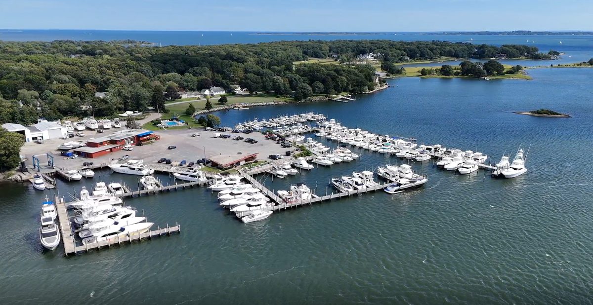An aerial view of a coastal marina illustrates the Class A boating assets added to Bain Capital Real Estate and BlueWater Marinas' expanding East Coast portfolio through the acquisitions of Mystic River Marina and Ripley Light Drystack Marina.