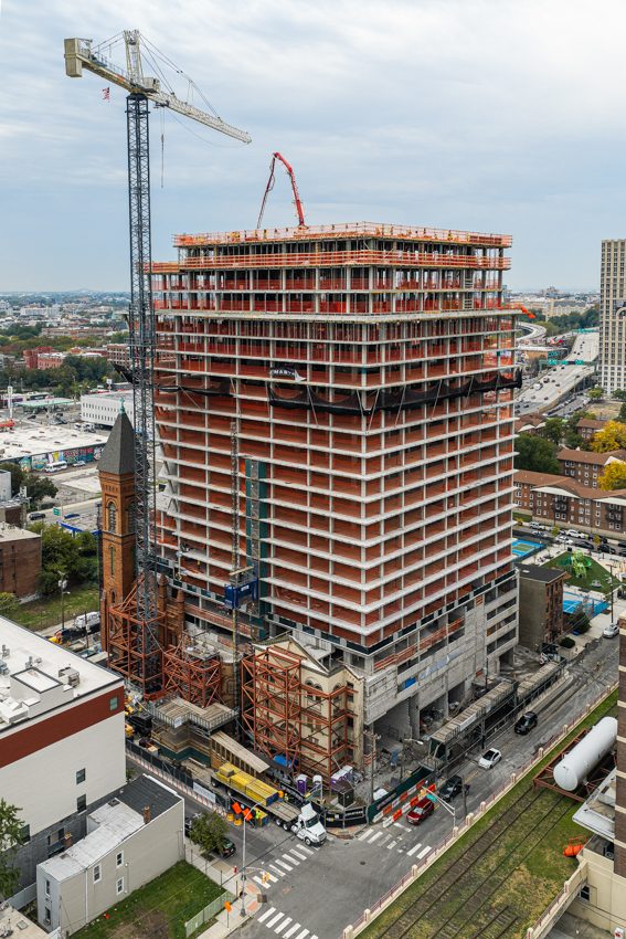 An aerial view shows The Lucy rising at 619 Grove St. in Jersey City, documenting the 444-unit tower's construction progress ahead of its 2028 completion.