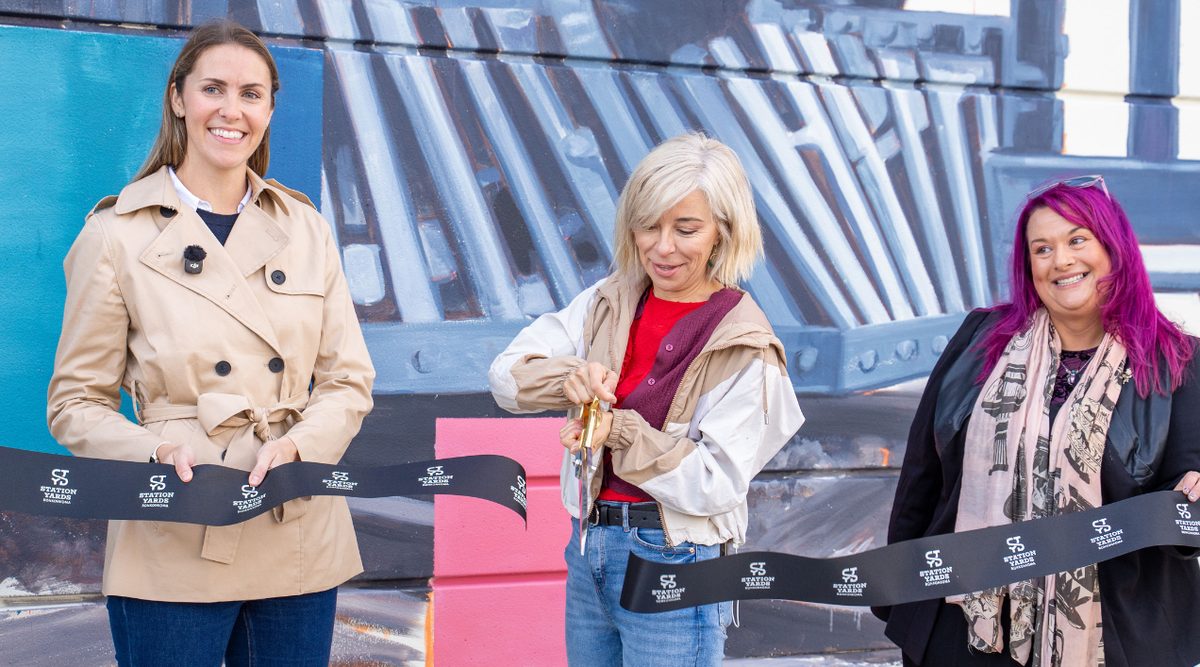 Lula Goce, Meaghan Coughlan Treat, and Beth Giacummo take part in a ribbon cutting for a new mural at Tritec Real Estate Company's Station Yards development in Ronkonkoma.